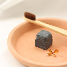 Load image into Gallery viewer, Dentifrice solide au charbon noir en cube, posé dans une coupelle avec brosse.