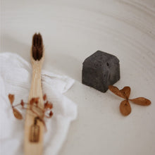 Load image into Gallery viewer, Dentifrice solide au charbon noir en cube, près d’une brosse à dents en bois.