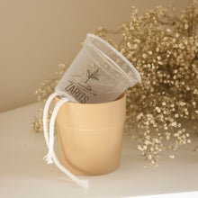 Charger l'image dans la galerie, Cache-pot beige avec sac en tissu beige noué sur le bord supérieur.

