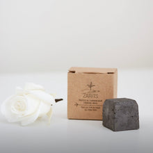 Load image into Gallery viewer, Masque solide au charbon : pain gris foncé, boîte kraft et fleur blanche à côté.
